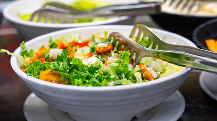 Special tongs in a salad of tomatoes, bell peppers and green lettuce leaves. Healthy eating concept