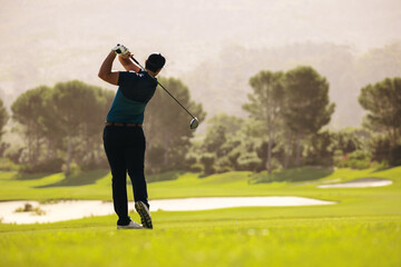 Male golfer swinging golf club with a powerful follow through on a sunny fairway