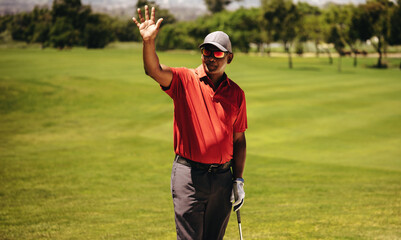 Golfer greeting with raised hand while resting during a match at the golf club.