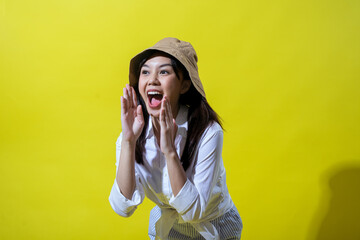 Asian woman enthusiastically calling out, wearing a beige bucket hat, white shirt, and striped...