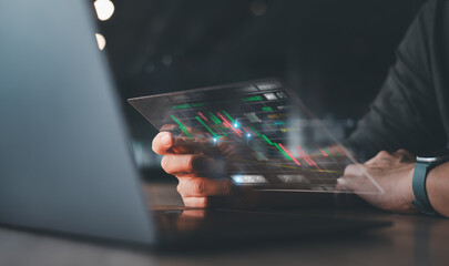 Close-up of a hand using a transparent digital screen displaying financial data and stock market charts in a modern setting.