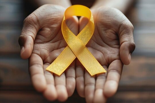 Hands holding a yellow gold ribbon representing Sarcoma Awareness, Bone cancer, childhood cancer awareness, and World Suicide Prevention Day in September. - Powered by Adobe