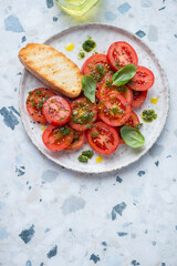Plate with sliced red tomatoes and basil oil, vertical shot on a white and blue granite background, high angle view, copyspace