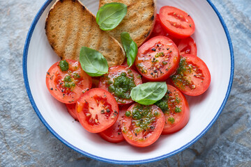 Tomato salad with basil oil, green basil and grilled ciabatta in a blue and white plate, middle close-up, horizontal shot