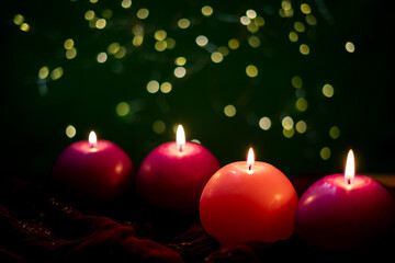  Four glowing Advent candles, symbolizing love, peace, joy, and hope, set against a green background with soft bokeh lights creating a serene and festive atmosphere