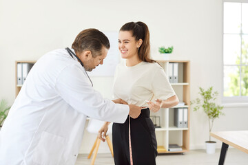 Obraz premium Male doctor, nurse doing measure waist using tape measure, taking young female patient body measurements, happy girl during examination on regular clinic check up for medical wellbeing, body care 