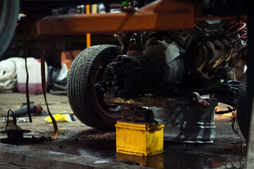 a mechanic disassembles an old dirty car engine on a red lift for repair and tuning