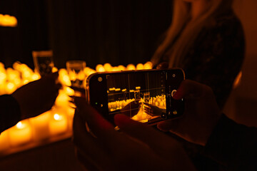 hands with phone taking video of symphonic orchestra on stage with lots of candles