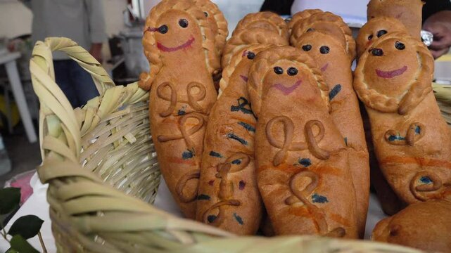 Slow motion zoom-in basket of traditional Ecuadorian guagua de pan with people preparing in kitchen, Day of Dead celebration