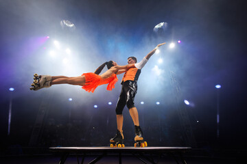 Young pair of acrobats, man and woman, on roller skates perform in a circus on a small round stage. © Studio Peace
