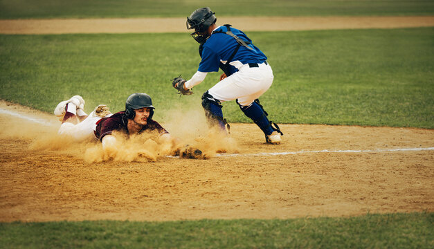 Intense baseball action as player slides home with dust cloud while catcher prepares for tag
