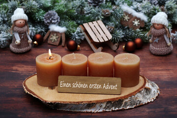 Dekoration zum ersten Advent: Adventskranz mit vier braunen Kerzen, kleinen Püppchen, Weihnachtsschmuck und der Beschriftung einen schönen ersten Advent.