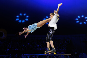 Young pair of acrobats, man and woman, on roller skates perform in a circus on a small round stage.