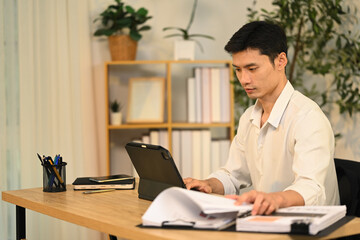 Fototapeta premium Concentrated adult businessman using digital tablet and reviewing documents at desk