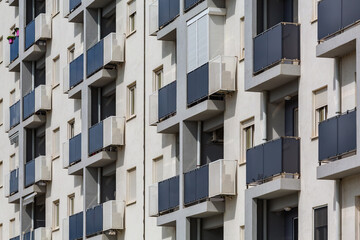 Fototapeta premium Modern apartment building facade with uniform balconies and minimalistic design. Features dark balcony railings contrasting with a light exterior