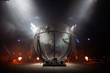 Dangerous show involving motorcyclists in circus. Stuntmen ride motorcycles in metal round cage.
