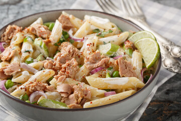 Creamy canned tuna salad with penne pasta, green peas, red onion and celery close-up in a plate on the table. Horizontal