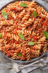 Bolognese pasta Fusilli with tomato sauce, ground minced beef, basil leaves closeup on the plate on the table. Vertical top view from above