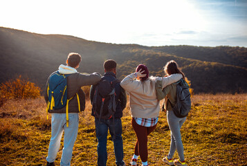 Smiling group of friends having fun while hiking together on hill at sunset.