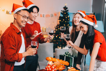 Group of young Asian man and women as friends having fun at a New Year's celebration, holding gift boxes standing by Christmas tree decoration, midnight countdown Party at home with holiday season.