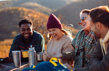 Group of friends sitting on the top of the hill at bench resting after hiking and drinking tea.