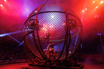 Dangerous show involving motorcyclists in circus. Stuntmen ride motorcycles in metal round cage.