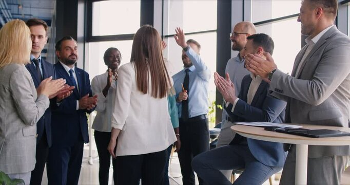 A group of business people in the company lobby greets a female colleague with applause. The concept of friendliness and cooperation in the team. Young businesswoman accepts congratulations