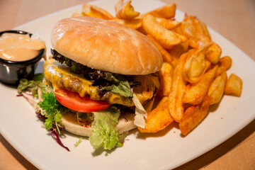 A juicy cheeseburger with lettuce, tomato, and sauce, served alongside seasoned fries on a white plate.