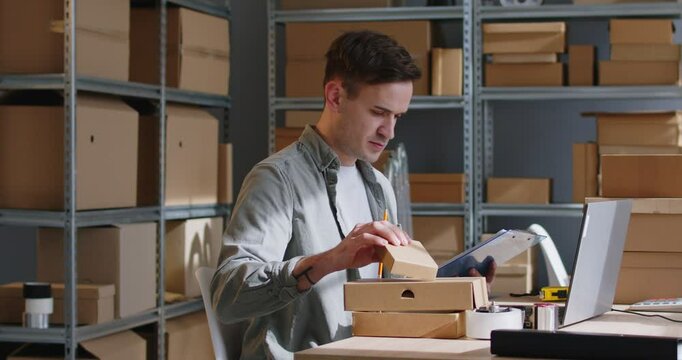 Businessman working in a parcel warehouse with a laptop, conducting inventory or processing orders for an online shop. Focus on the task showcases commitment to storage management and order process.