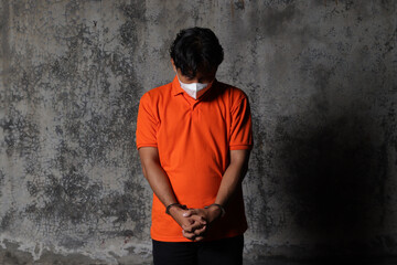 Arrested criminal suspect was wearing an orange shirt with his hands in handcuff, dramatic light...