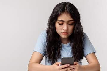 Naklejka premium Girl is using smartphone in gray on white . w female phone concept. young girl with her hands up and smartphone in her hand at table with grey . a young girl with her hands on at a smartphone sitting.