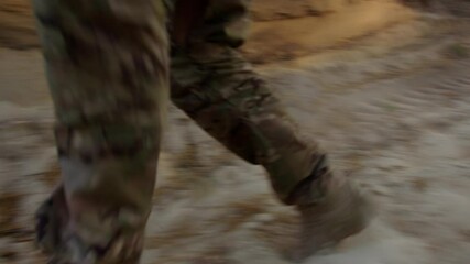 Close-up of a soldier's boots running through a sandy trench, kicking up dust with every step. The video captures the intensity and physical demands of military operations in rugged terrain