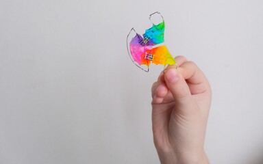 A dental plate for children of rainbow color. The child holds orthodontic braces in his hands to align the teeth and expand the jaw.