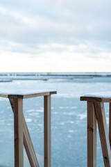 Serene winter photo, taken in Tallinn, Estonia, captures a view over an icy body of Baltic Sea in Haven Kakumäe harbor. In the foreground simple wooden railing with light snow dusting. 