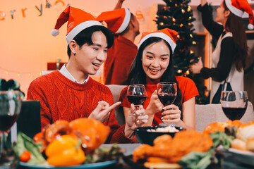 Group of young Asian man and women as friends having fun at a New Year's celebration, holding gift boxes standing by Christmas tree decoration, midnight countdown Party at home with holiday season.