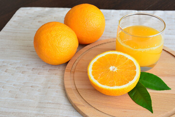 three oranges and a glass of orange juice are on a cutting board  