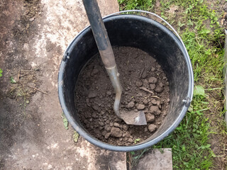 Close-up of a plastic bucket with soil in home garden in summer. Gardening and work in backyard