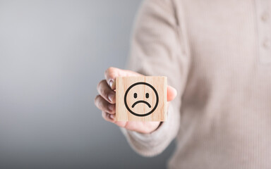 Man holds a wooden block with a sad face, symbolizing feelings of sadness or emotional challenges. This image reflects the concept of acknowledging and addressing negative emotions