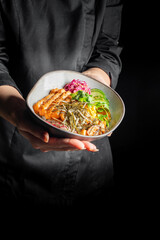 person holds a plate with a colorful assortment of grilled meat, vegetables, and grains, showcasing a vibrant and healthy meal. dish is well-presented, emphasizing culinary art and nutritious eating.