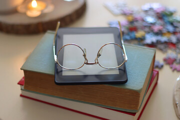 Colorful jigsaw puzzle pieces, books, tablet, glasses, cookies, berries, cup of tea or coffee, glass of juice and lit candles on the table. Hygge in pastel colors. Selective focus.