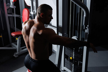 Back of bodybuilders exercise with lifting weights on an exercising machine in gym or fitness club.