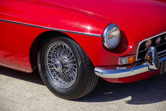 Red mgb classic car exhibiting chrome spoke wheel and headlight