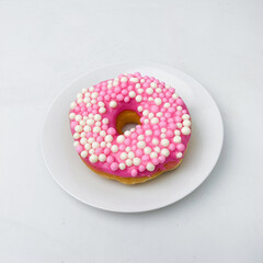 Bright and colorful pink donut decorated with crunchy white and pink pearl sprinkles. A delicious and eye-catching dessert for any celebration.