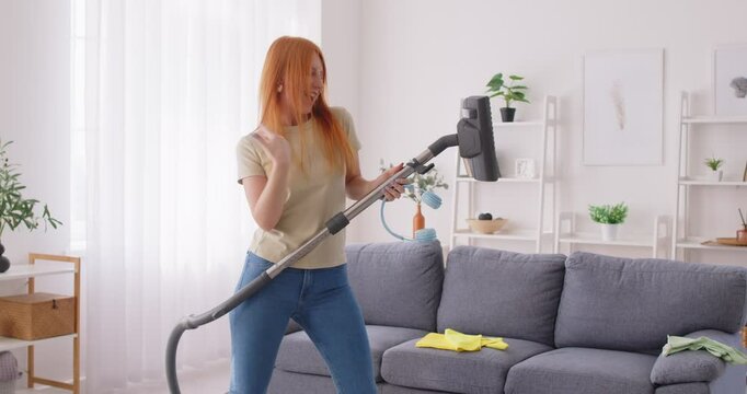 Satisfied Caucasian housewife dancing to music while vacuuming during housecleaning at home. Fun and joy of household chores as she enjoys cleaning and keeping domestic space tidy.