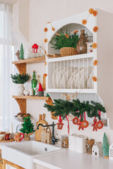 Beautifully arranged kitchen shelves decorated with spruce garlands, Christmas tree and ornament items. Interior of kitchen, white counters decorated for seasonal winter holidays, festive atmosphere