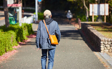 秋の昼の道路で歩く一人のシニア男性の姿