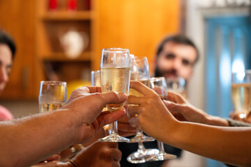 Friends raising glasses of champagne, celebrating party together in a cozy home kitchen