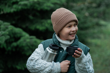 Cute little boy decorating Christmas tree in the forest and drinking hot tea. Winter holidays, picnic.