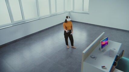Asian female designer in virtual reality headset uses augmented reality interior design app and wireless controllers to build office workspace with 3D furniture and modern equipment. 3D visual effects © Framestock