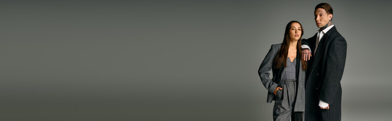 A fashionable young couple stands together, exuding charm and sophistication in their sleek outfits.